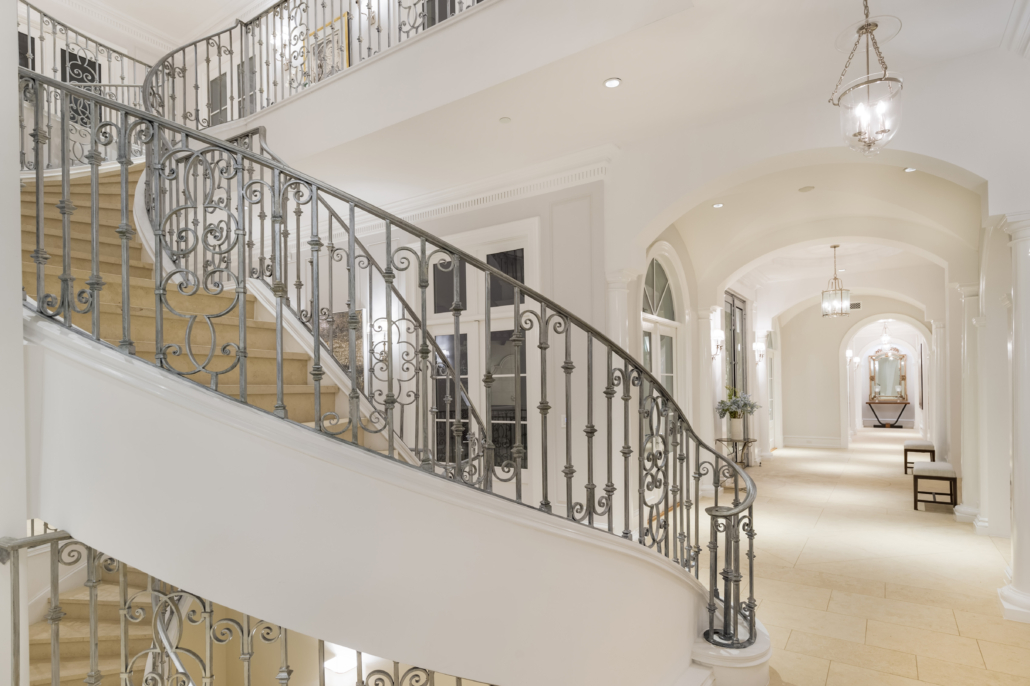 A curved stone staircase with ornate metal balustrades and a bright double-height entrance