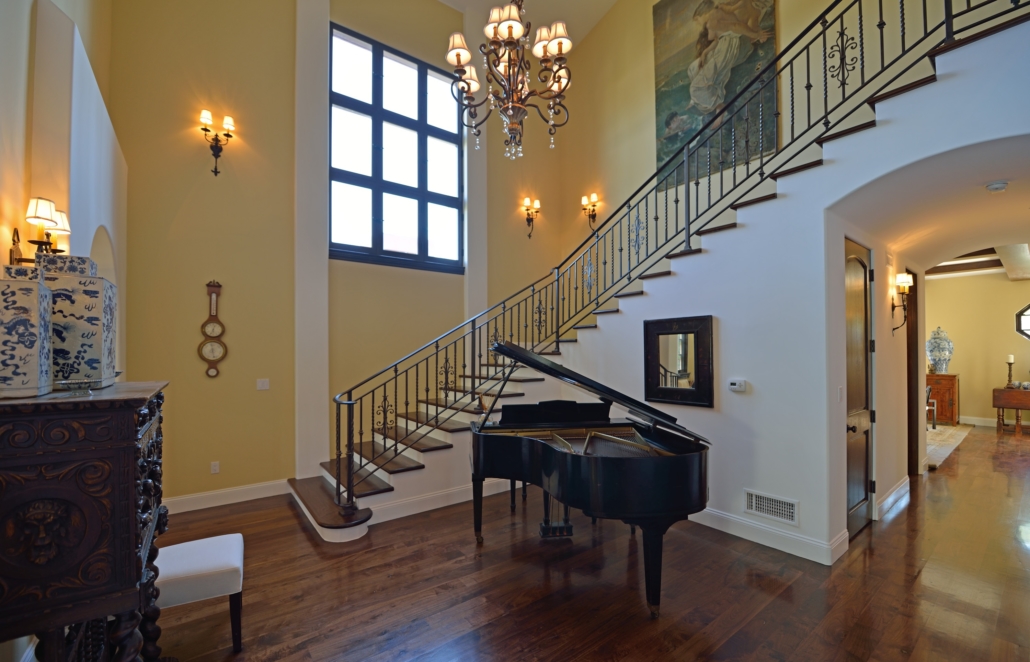 Curved staircase with dark metal railings in a double-height entrance with a grand piano
